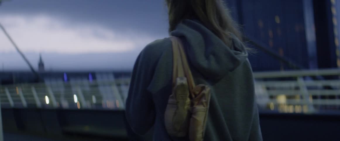 Woman walks across a city bridge at dusk