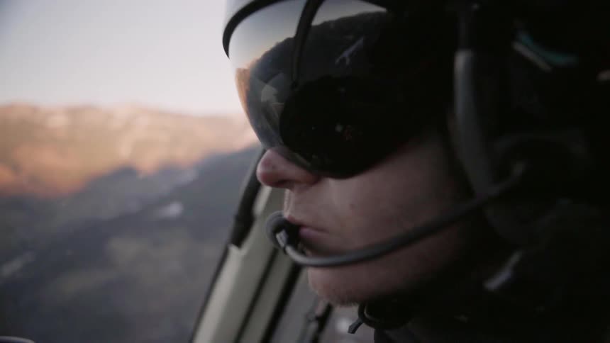 A pilot flies a helicopter over mountains