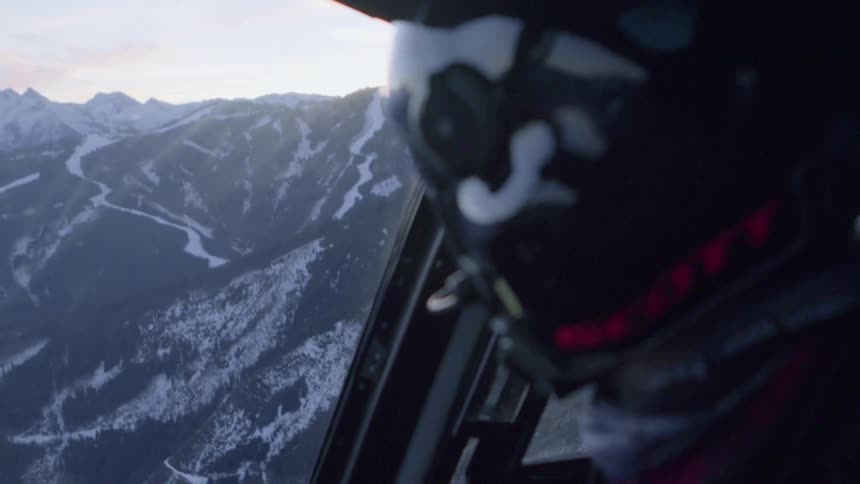 A helicopter is piloted over snowy mountains