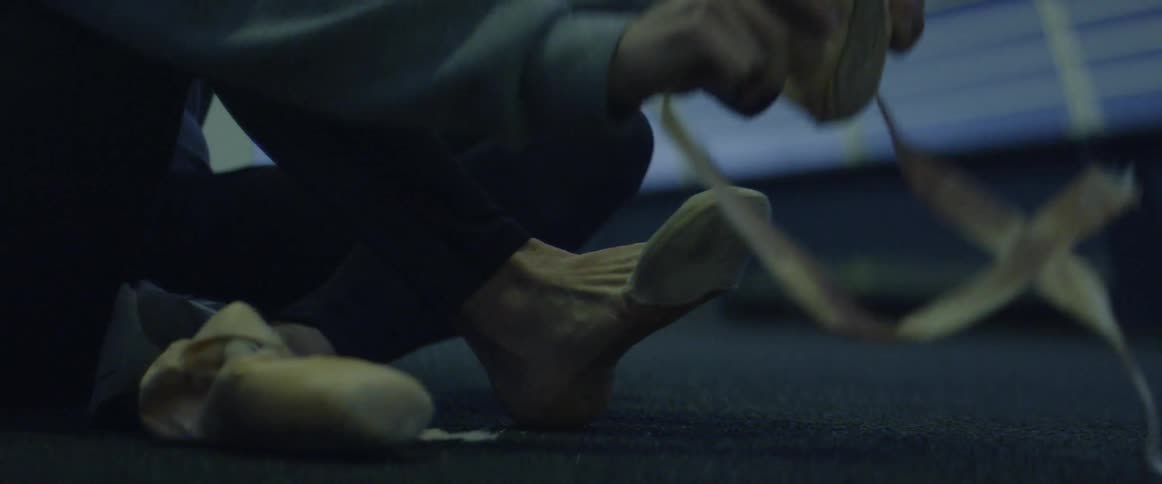 A woman is putting on ballet shoes in the dark room