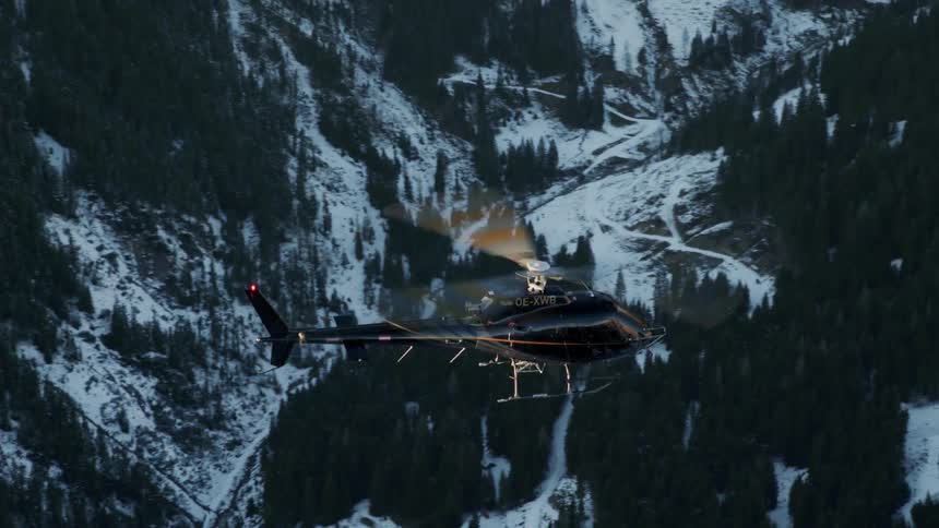 A helicopter flies over snowy mountains