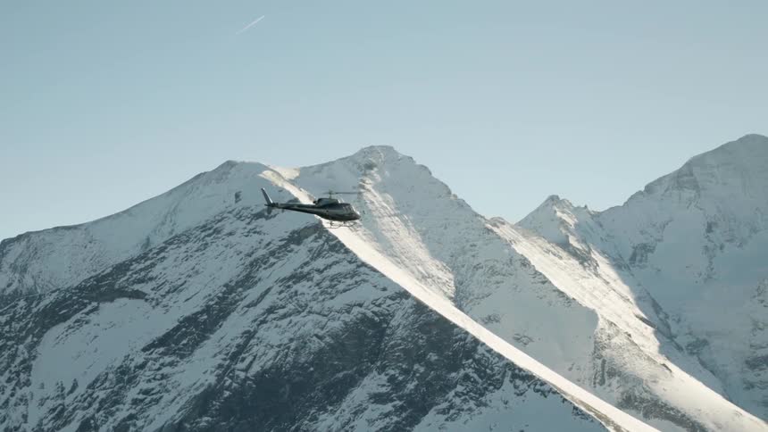 A helicopter flies up near the tall snowy mountains