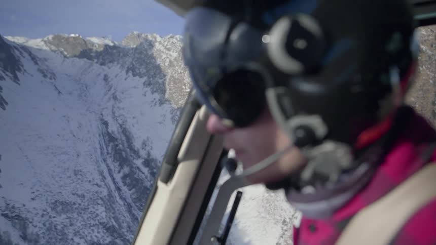 A helicopter pilot flies by a mountain ridge