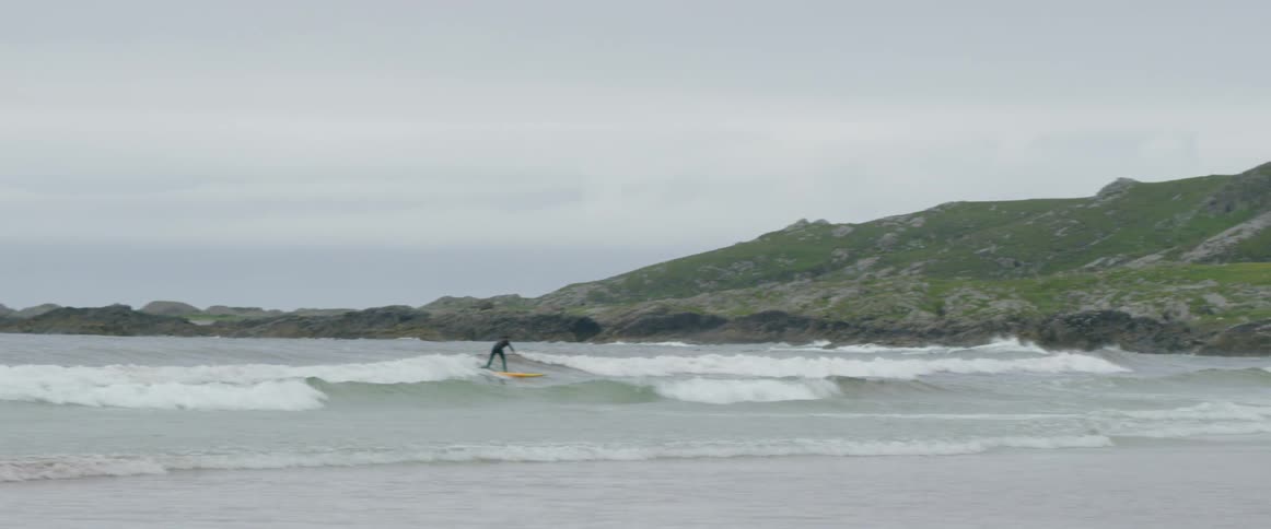 A surfer rides a wave towards the shore