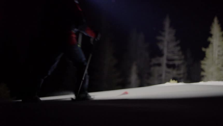 A man with a powerful flashlight is walking through the snowy woods at night