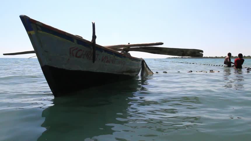 People pulling in a net in the water near a boat