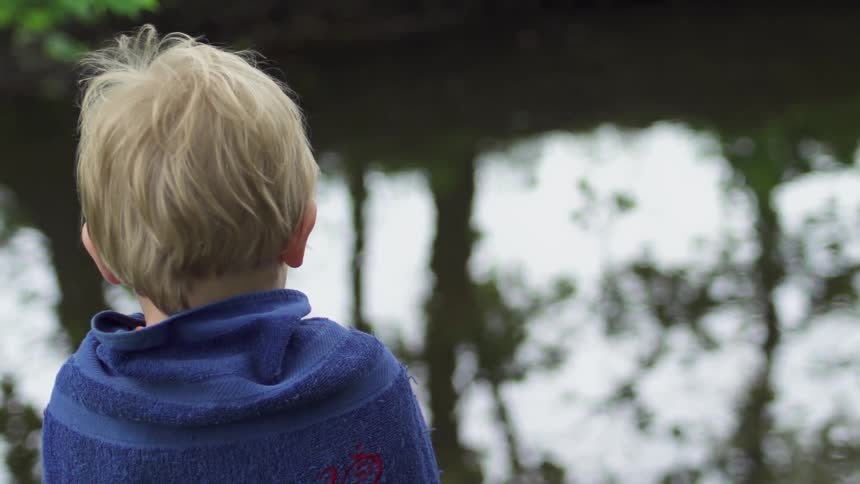 A young boy sits next to the water