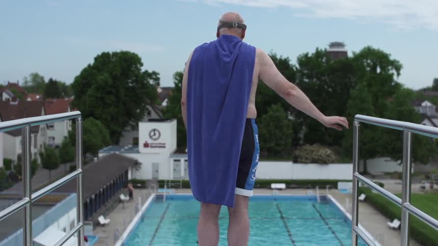 A man wearing a cape stands atop a diving platform