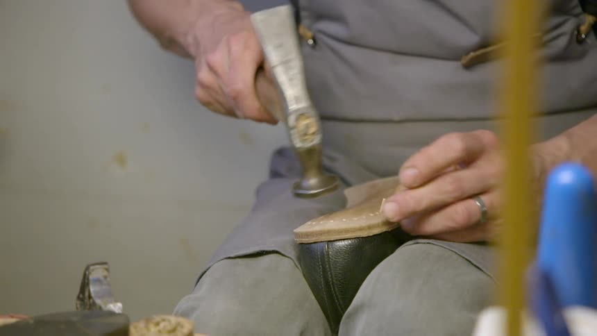 A shoe maker hammers a nail into the sole of a shoe