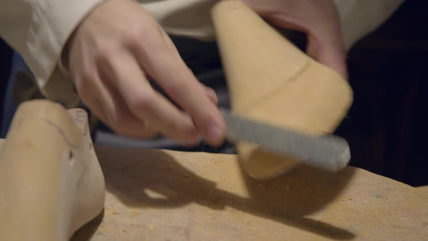 A cobbler is sanding a shoe form