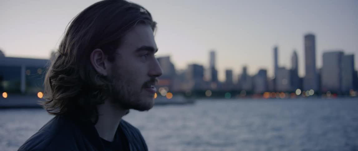Man talks while standing next to city river at dusk
