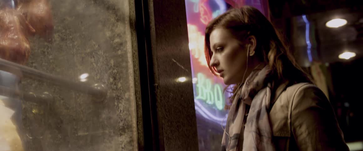 Woman stands outside of a brightly lit building at night