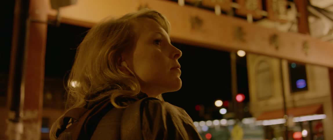 A blond haired woman puts on earbuds outside at night