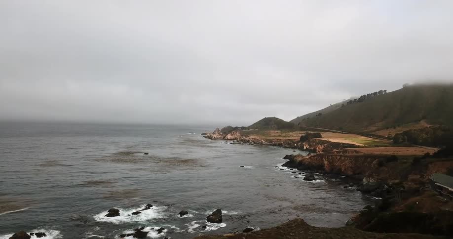 Waves are crashing around rocks on a foggy day