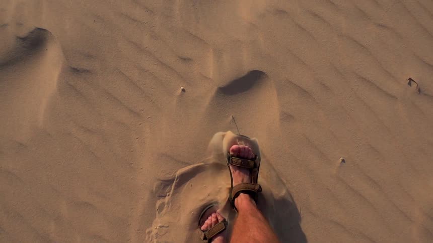 A man is walking through the desert sand wearing sandals