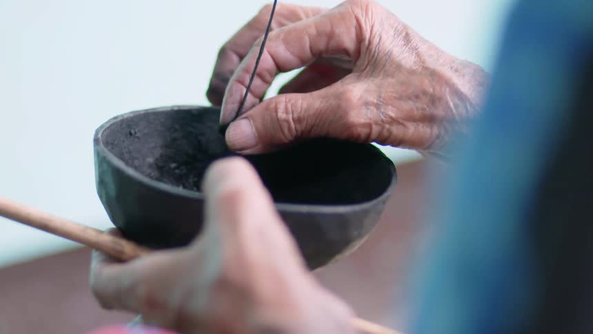 An elderly woman dipping a quill in a bowl of ink