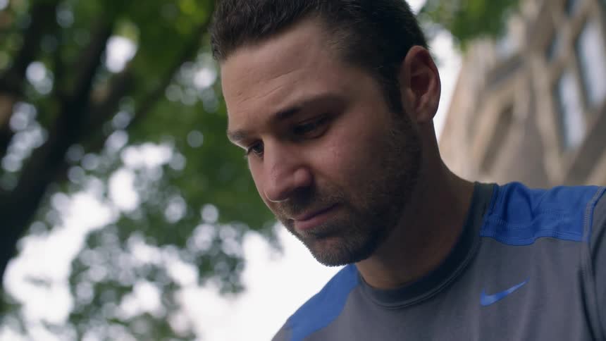 A man looks down outside under a tree