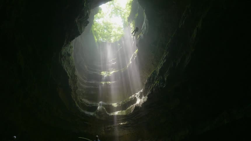 A person dangles from a rope as they are descending into a cavern during the day