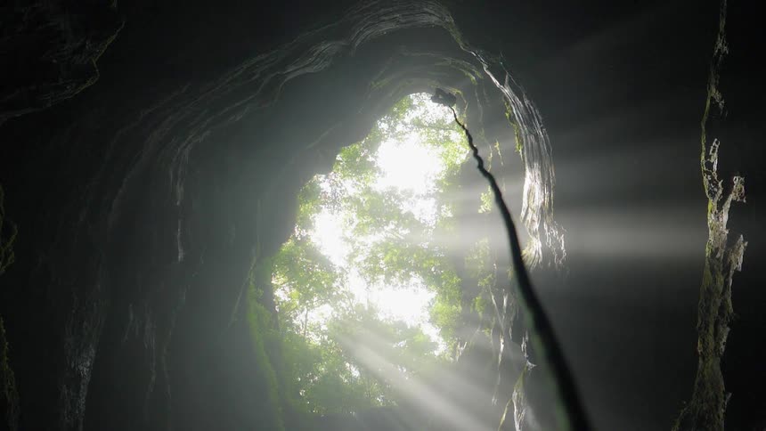 A rope is dangling down from the opening of a cave