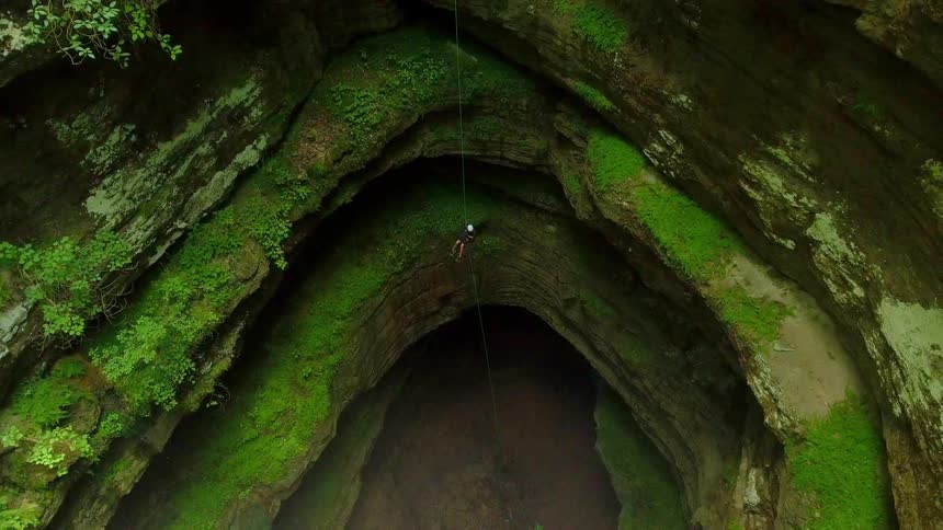 A person going down a large natural cavern in rappel
