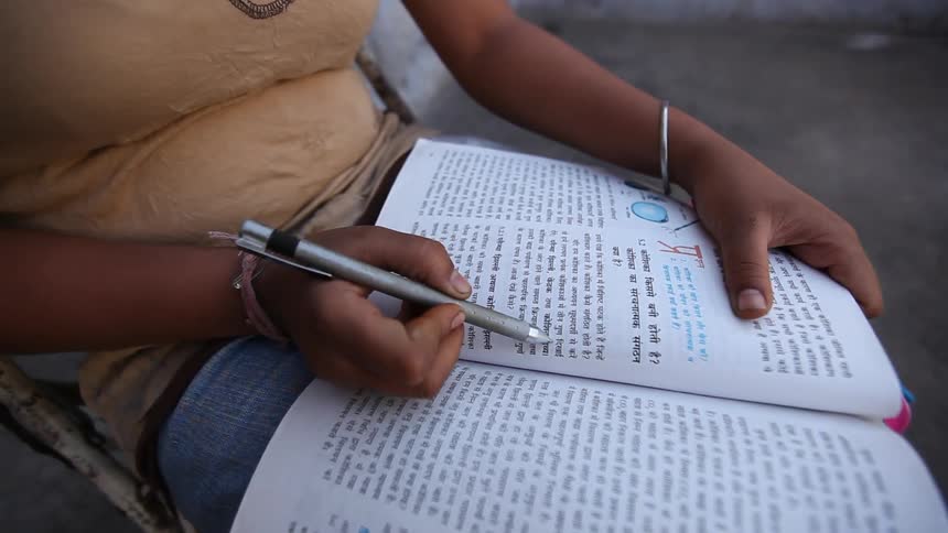 A woman uses a pen as a guide while reading a textbook