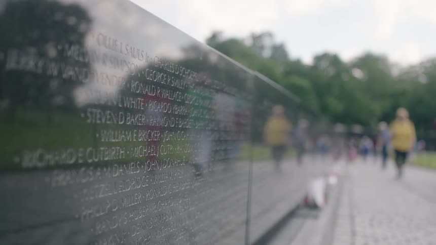 People walk by a granite monument etched with names during the day