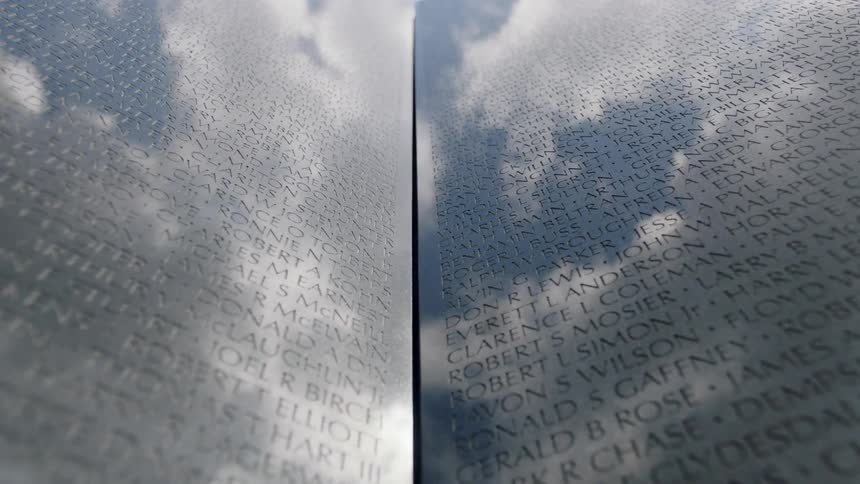 Names engraved on a large wall with clouds reflecting