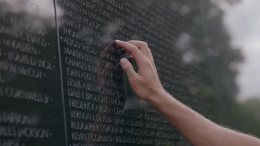 A man is touching the names etched onto a war memorial during the day