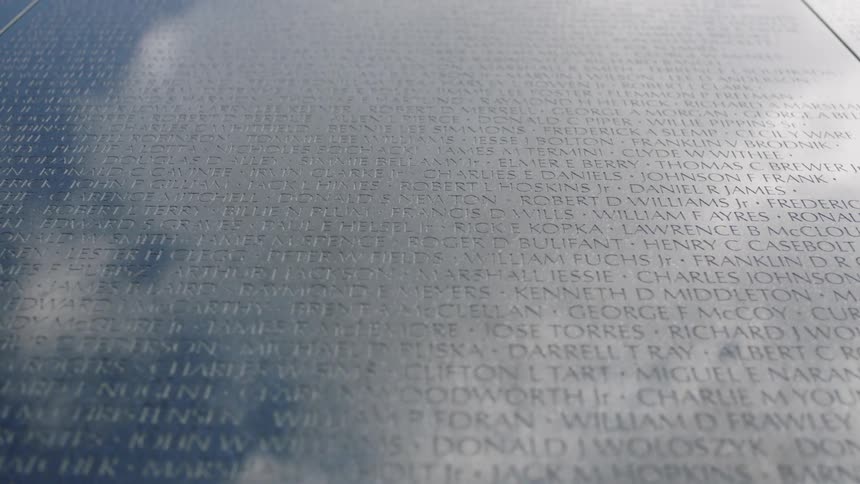 Names engraved on a large wall with clouds reflecting