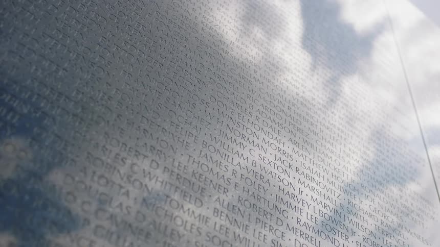 A cloudy sky is reflecting in a monument etched with names