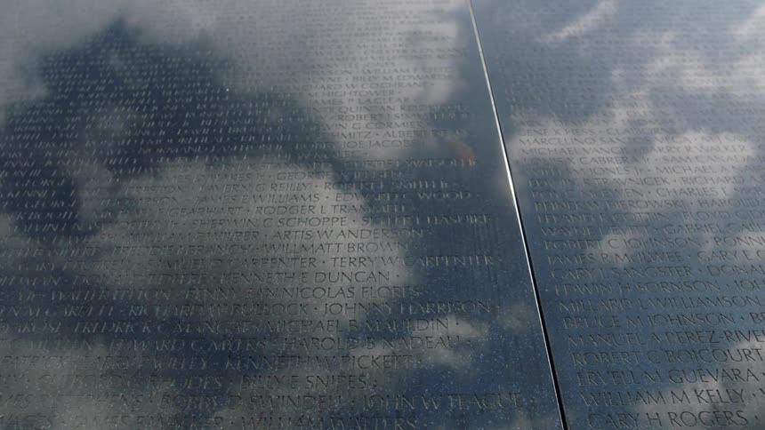 Names engraved on a large wall with clouds reflecting