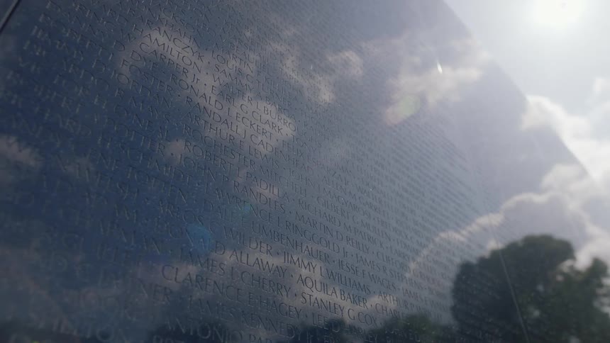 The sun and clouds are reflected off of a military personnel monument