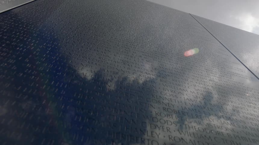 Names engraved on a large wall with clouds reflecting