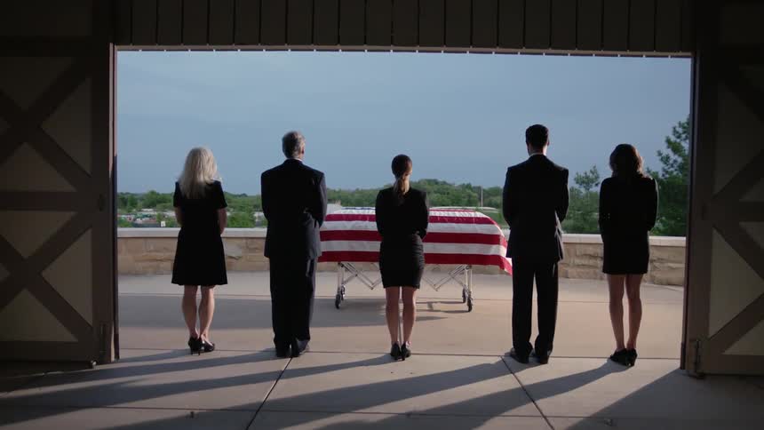 People grieve by a flag draped casket