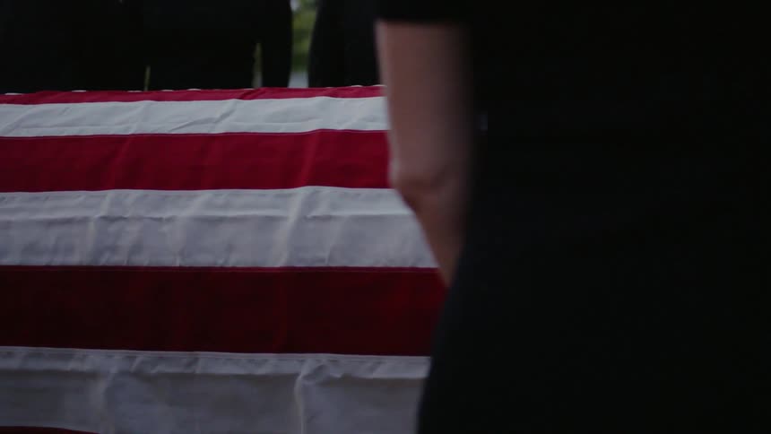 An american flag is wrapped over a casket at a funeral