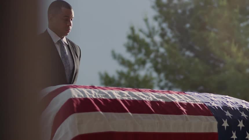 A man grieves next to a flag draped casket