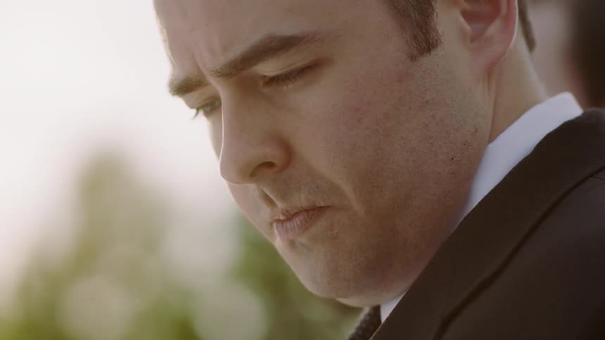 A man in suit looks down and blinks