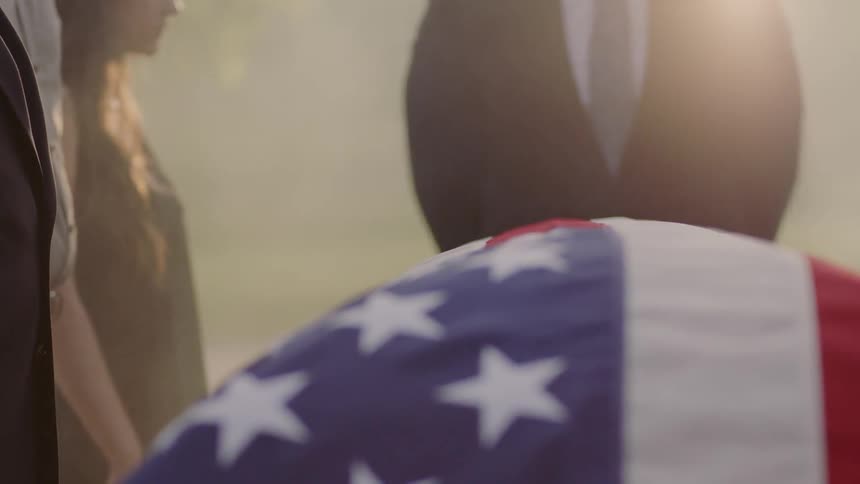 A group of people are gathered around a american flag covered coffin