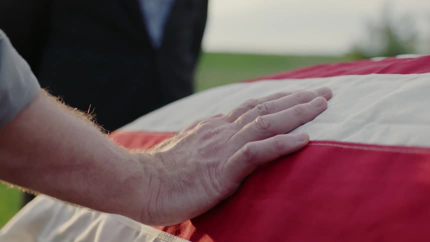 A man places his hand on a flag draped casket
