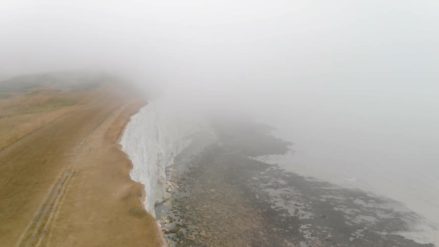 A foggy cliff overlooks the ocean below