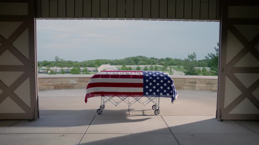 An american flag covered coffin is framed by a doorway