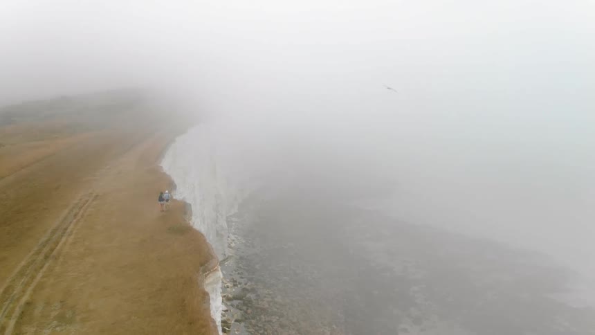Two people are standing on the edge of a foggy cliff