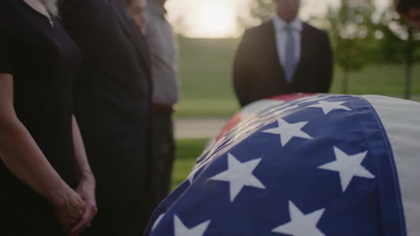An american flag is wrapped over a casket at a funeral