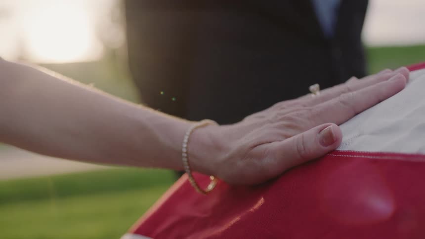 A woman places her hand on a flag draped casket
