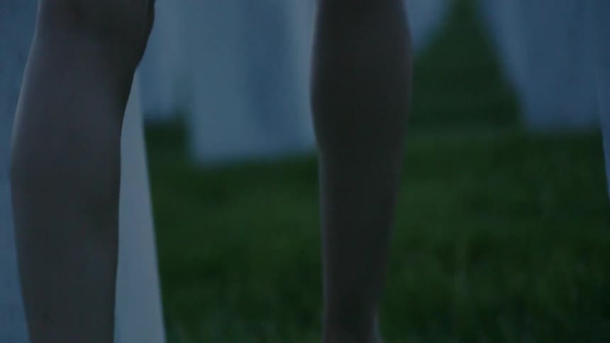 A woman in heels is walking pass tombstones carrying flowers