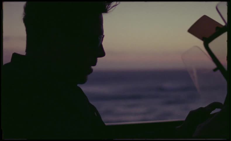 A man is sitting in his convertible next to the ocean