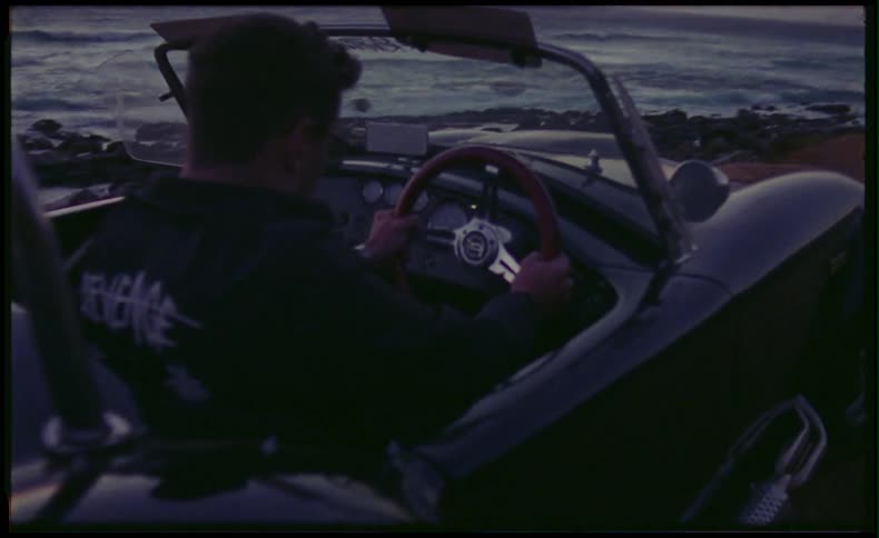 Man sitting in classic sports car by the beach at dusk