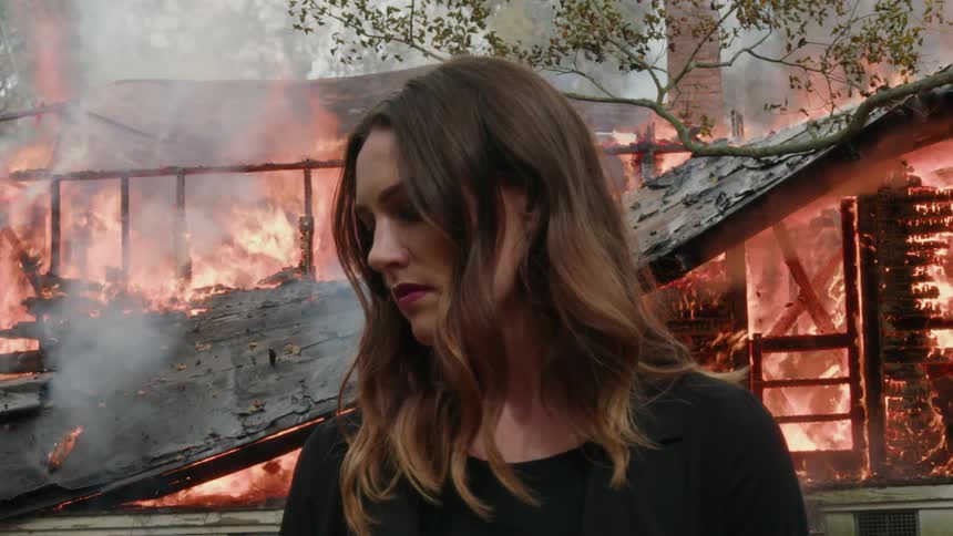 A girl is standing in front of a burning house as the roof collapses