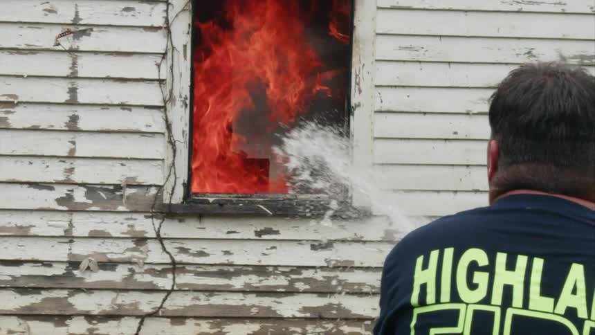 A firefighter sprays water through the window of a burning house
