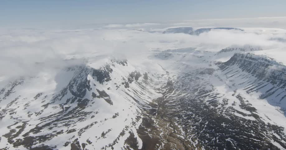 Light clouds hover above snow covered mountains